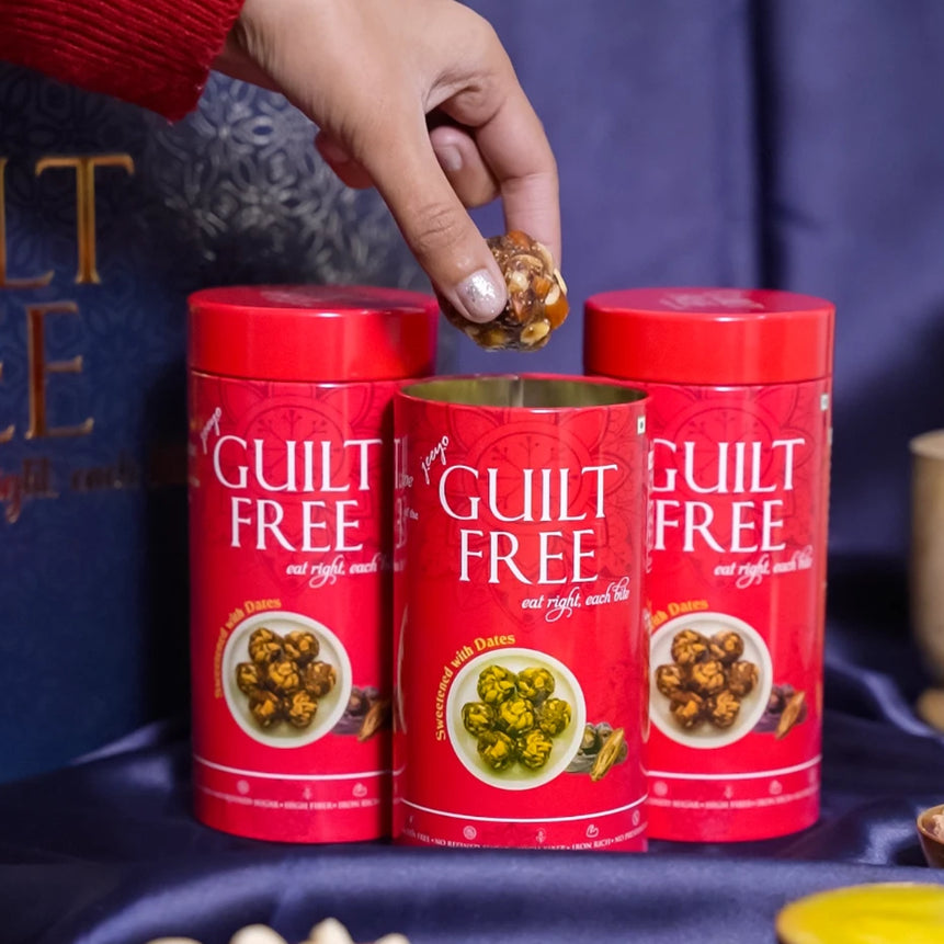 A person's hand reaching for a Guilt Free Luxe Bites container with various snacks like nuts and chips displayed in front.